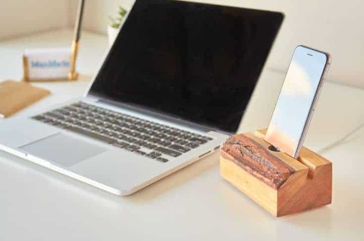 a wooden slab stand for phoe charging next to a laptop cimputer