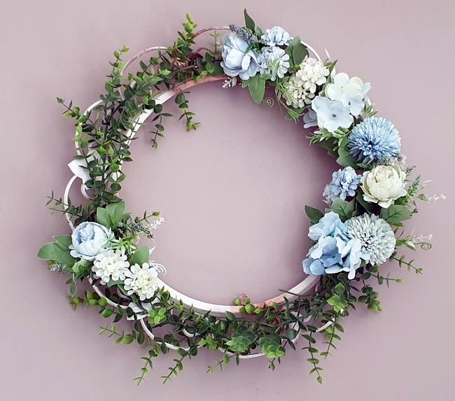 DIY summer wreath made with faux eucalyptus garland and blue and green faux flowers hanging on the wall