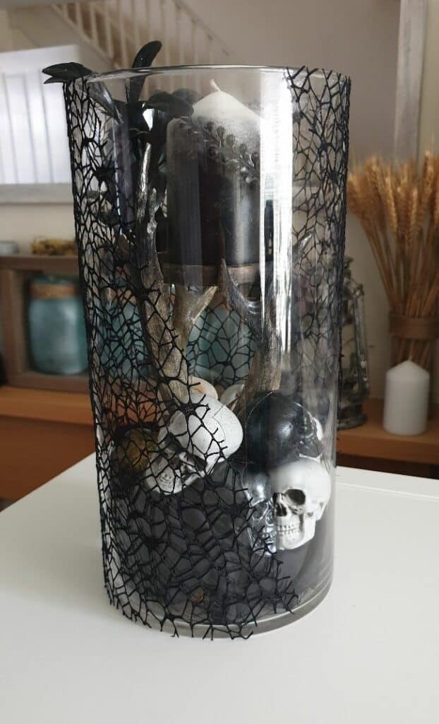 diy halloween decor centerpiece made with a glass vase, antler candle holder and small plastic skulls at the bottom