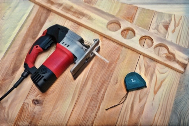 A jigsaw lying on a wooden surface next to a wooden plank with cut-out circle holes.